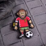 Klett-Patch von Gorillnaldo, fest auf einer grauen Klettfläche, zeigt den Gorilla in einer Fußballaktion.