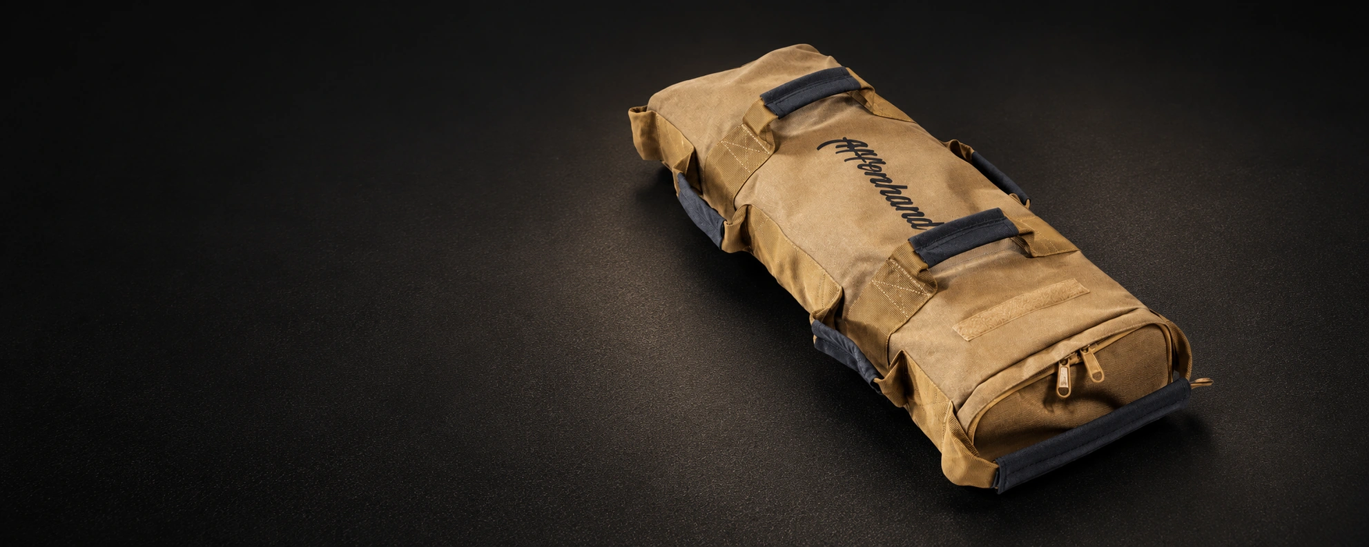 Sandfarbener Affenhand Fitness-Sandsack mit schwarzen Griffen auf mattem schwarzem Gummiboden.