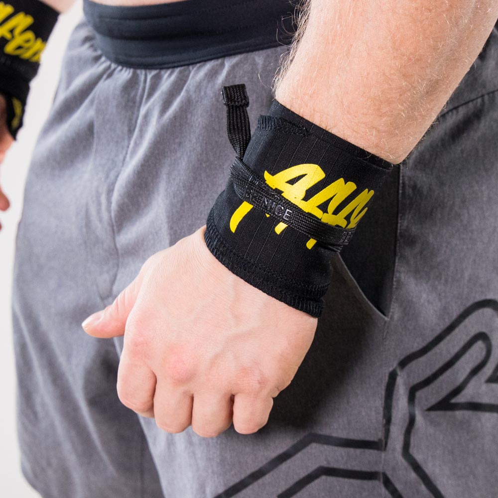 Nahaufnahme einer Person, die Affenhand Handgelenkbandagen in Schwarz-Gelb trägt, mit dem gelben Schriftzug „Affenhand“ auf schwarzem Stoff.