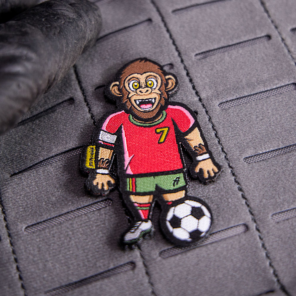 Klett-Patch von Gorillnaldo, fest auf einer grauen Klettfläche, zeigt den Gorilla in einer Fußballaktion.