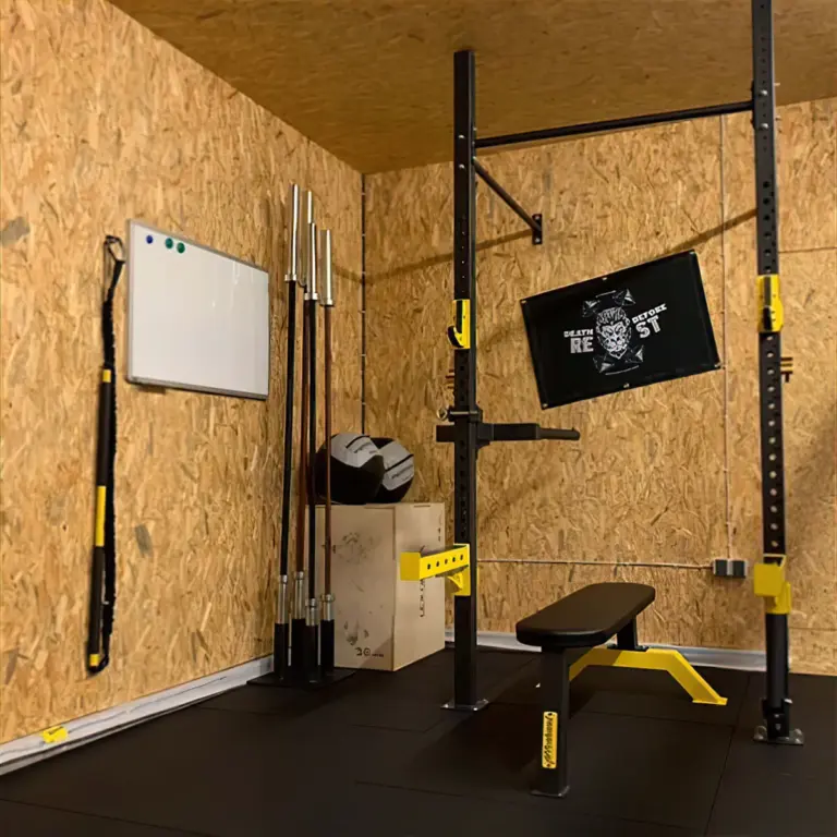 Individuelles Homegym mit schwarzem Rig, gelben Ablagen, Hantelbank und Gummiboden.