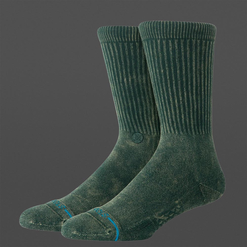 Zwei Stance Icon Dyed Pine Socken in Tannengrün mit leicht verwaschener Textur, geripptem Schaft und dezentem Logo, auf grauem Hintergrund.