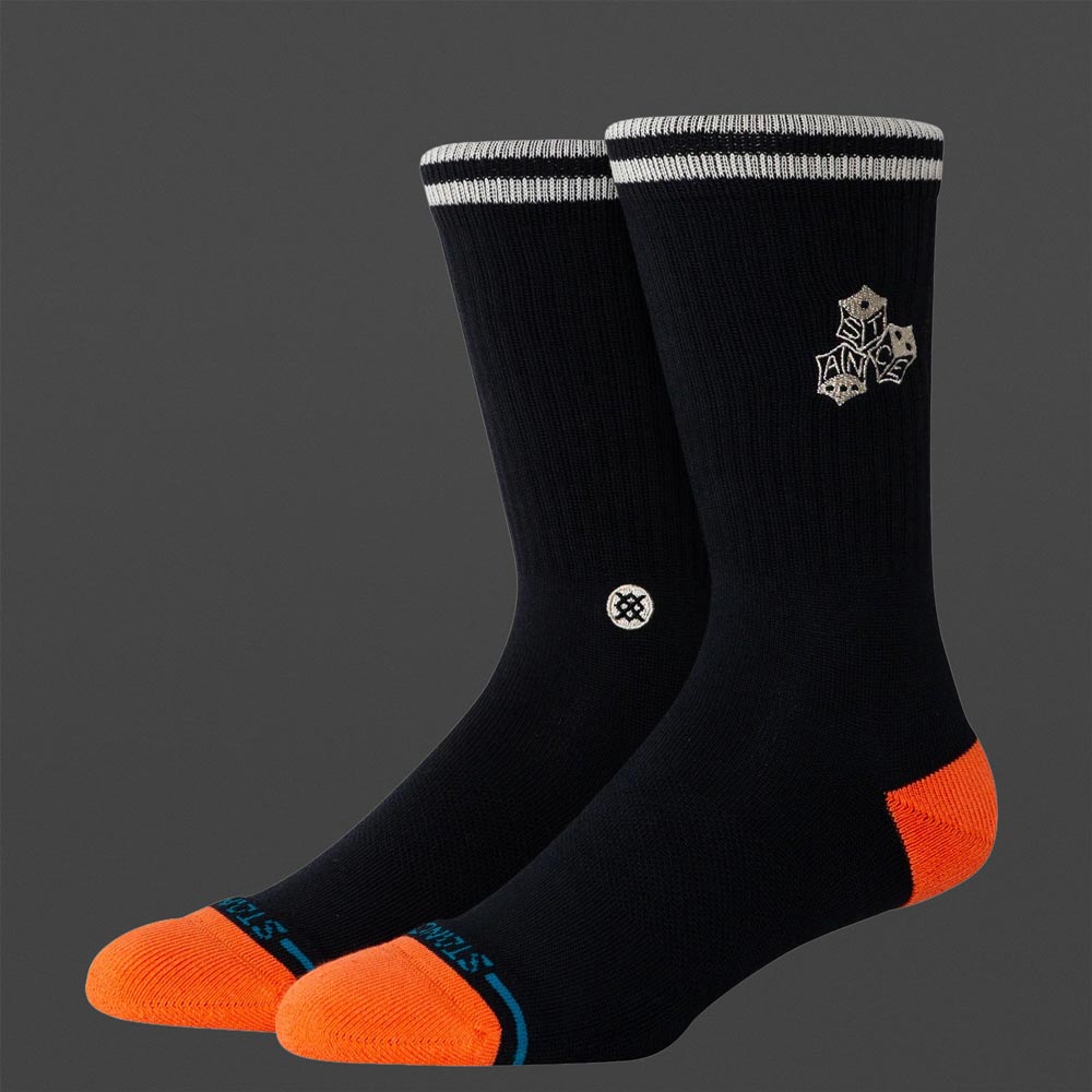 Zwei Stance High Roller Socken in Schwarz mit orangefarbener Zehen- und Fersenpartie, weißem Doppelstreifen am Bund und Stance-Logo seitlich, auf grauem Hintergrund.